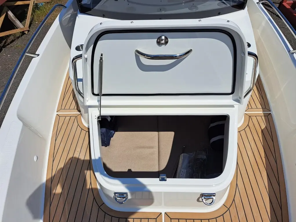 Boat interior showing a storage compartment with an open lid, on wooden flooring, under bright sunlight.